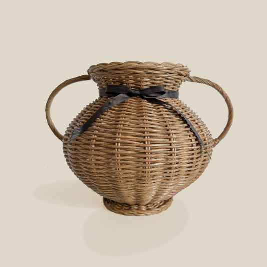 Kulplu el yapımı rattan vazo, siyah kurdele ile bağlanmış, yayvan formlu. Modern ahşap yemek masası üzerinde, kuru otlarla dekore edilmiş